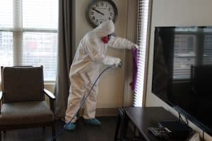 a suited-up team member using sanitation equipment in an apartment.